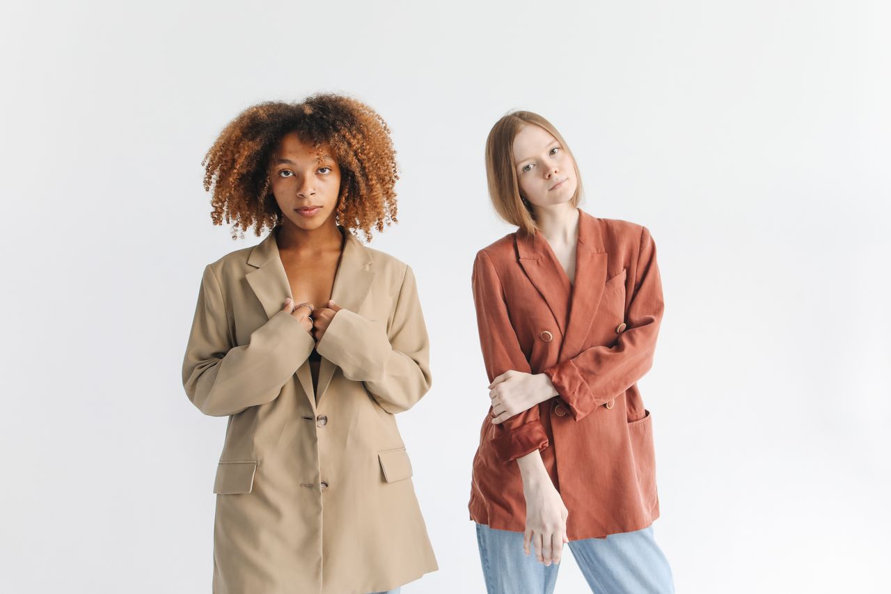 journey Two women modeling fashionable blazers in a studio setting with a white backdrop.